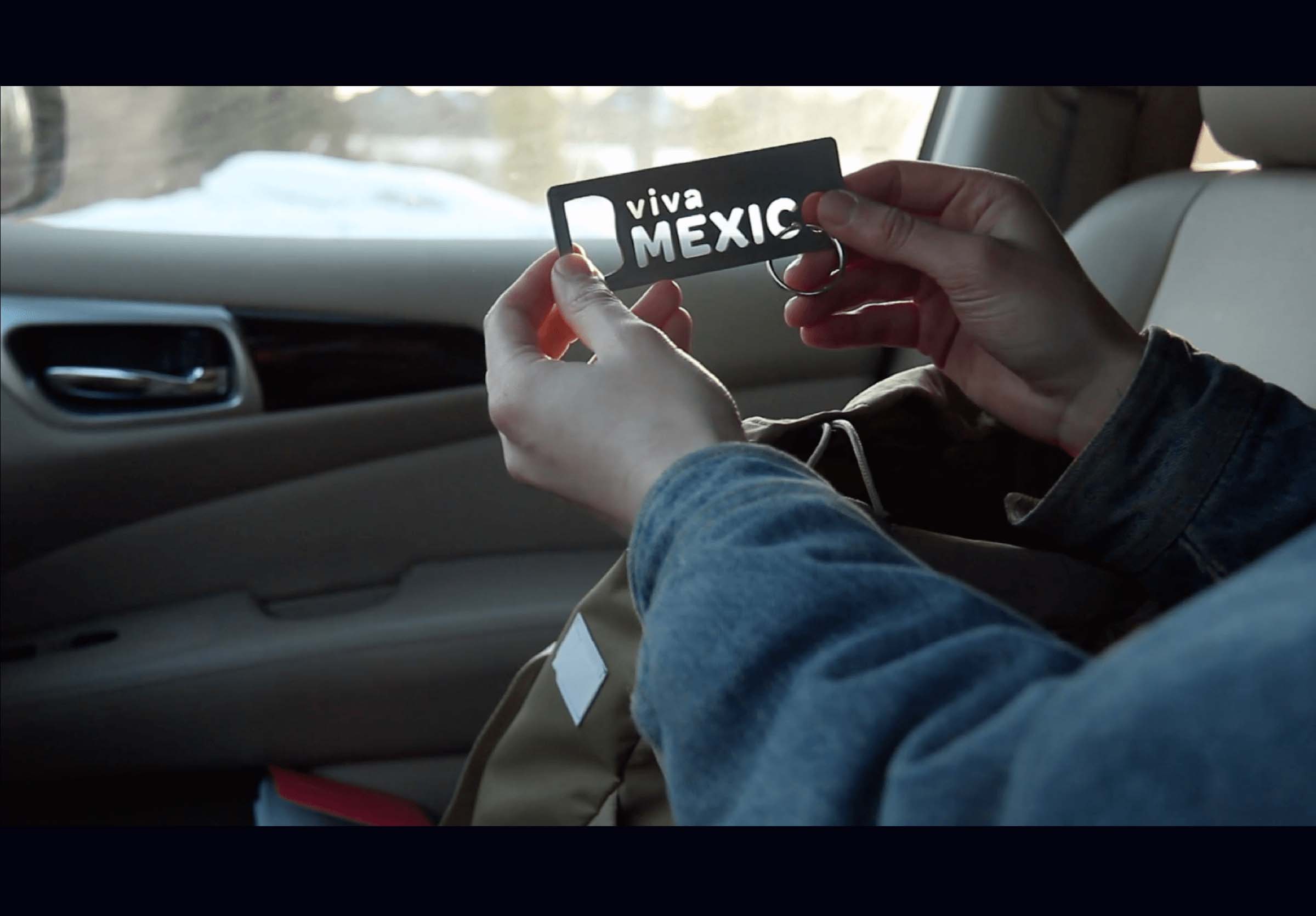 Hands in a car holding up a metal bottle opener saying viva Mexico